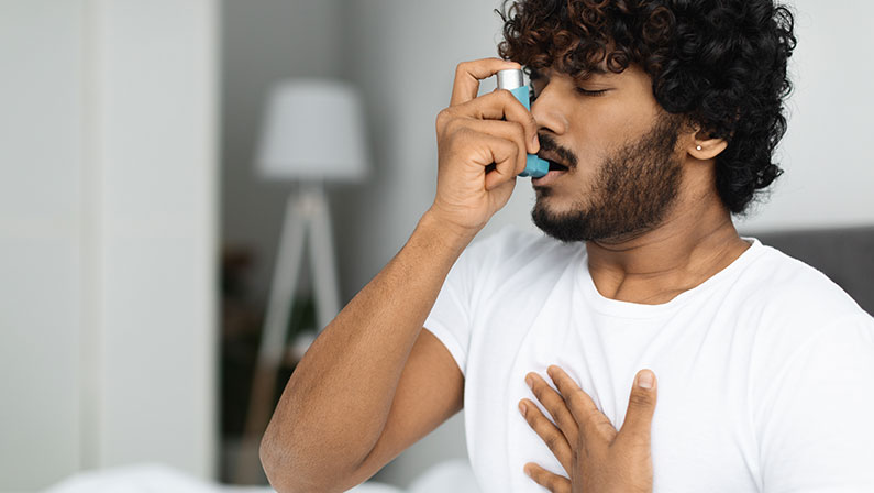 Guy suffering from asthma, using inhaler in bed.