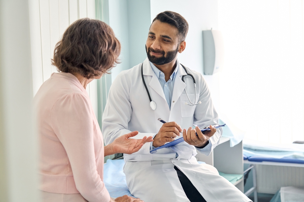 Professional physician wearing white coat talking to mature woman.
