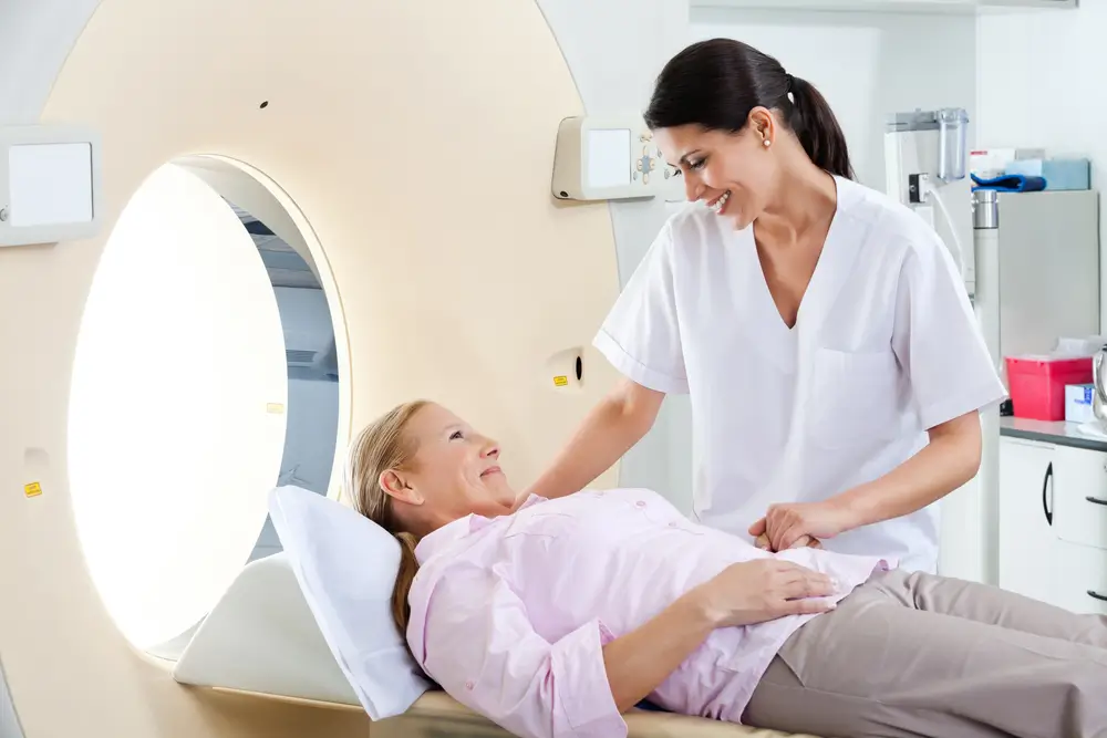 Radiologic technician smiling at mature female patient lying on a CT Scan bed
