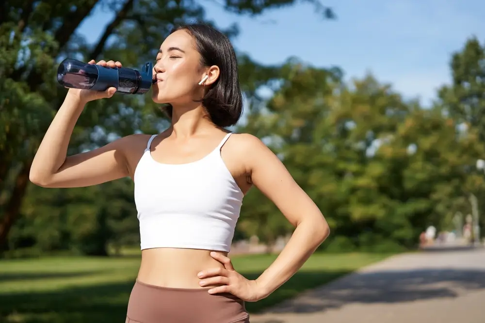 Smiling asian fitness girl drinks water, workout in park, stay hydrated during jogging training session.