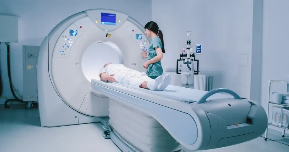 Woman is lying down at CT scanner bed. 