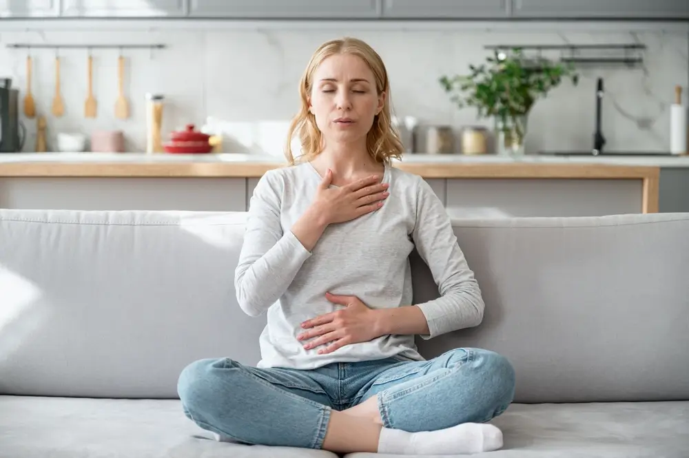 Woman sitting on couch and doing calming breathing exercises after panic attack.