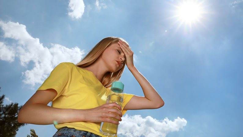 Woman with bottle of water suffering from heat stroke outdoors