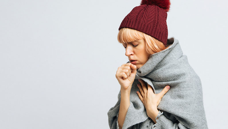 Cute sick young teen woman in red hat, wrapped in warm scarf coughing, closed eyes.Female feeling the first symptoms of illness.Bronchitis, upper respiratory infection concept.Moist cough, laryngitis