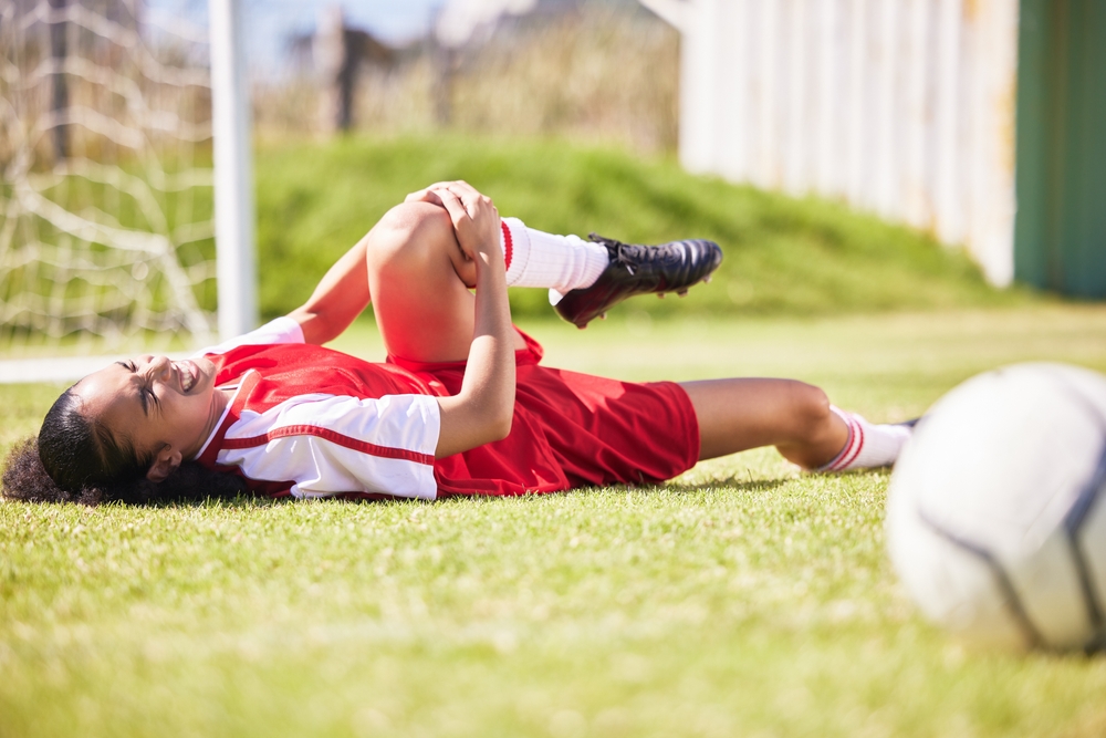 njured, pain or injury of a female soccer player lying on a field holding her knee during a match