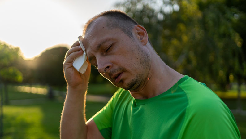 Overheated sweaty middle aged man suffering from heat stroke or high temperature, using paper napkin in summer park.