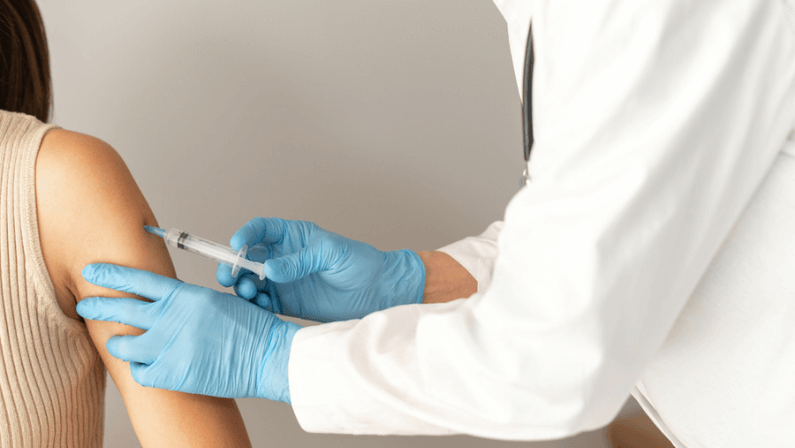 Close up of a healthcare professional doctor wearing medical sterile gloves, holding a syringe, injecting a shot of covid-19 vaccine to a patient. Immunization and prevention concept