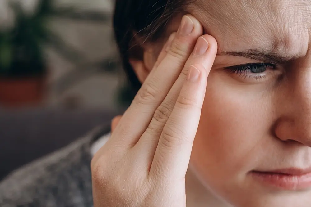 Close up of frustrated upset young brunette woman 20s coping with headache migraine concept feel anxiety pain pressure, mental stress, panic attack touching aching sore head sitting on couch at home